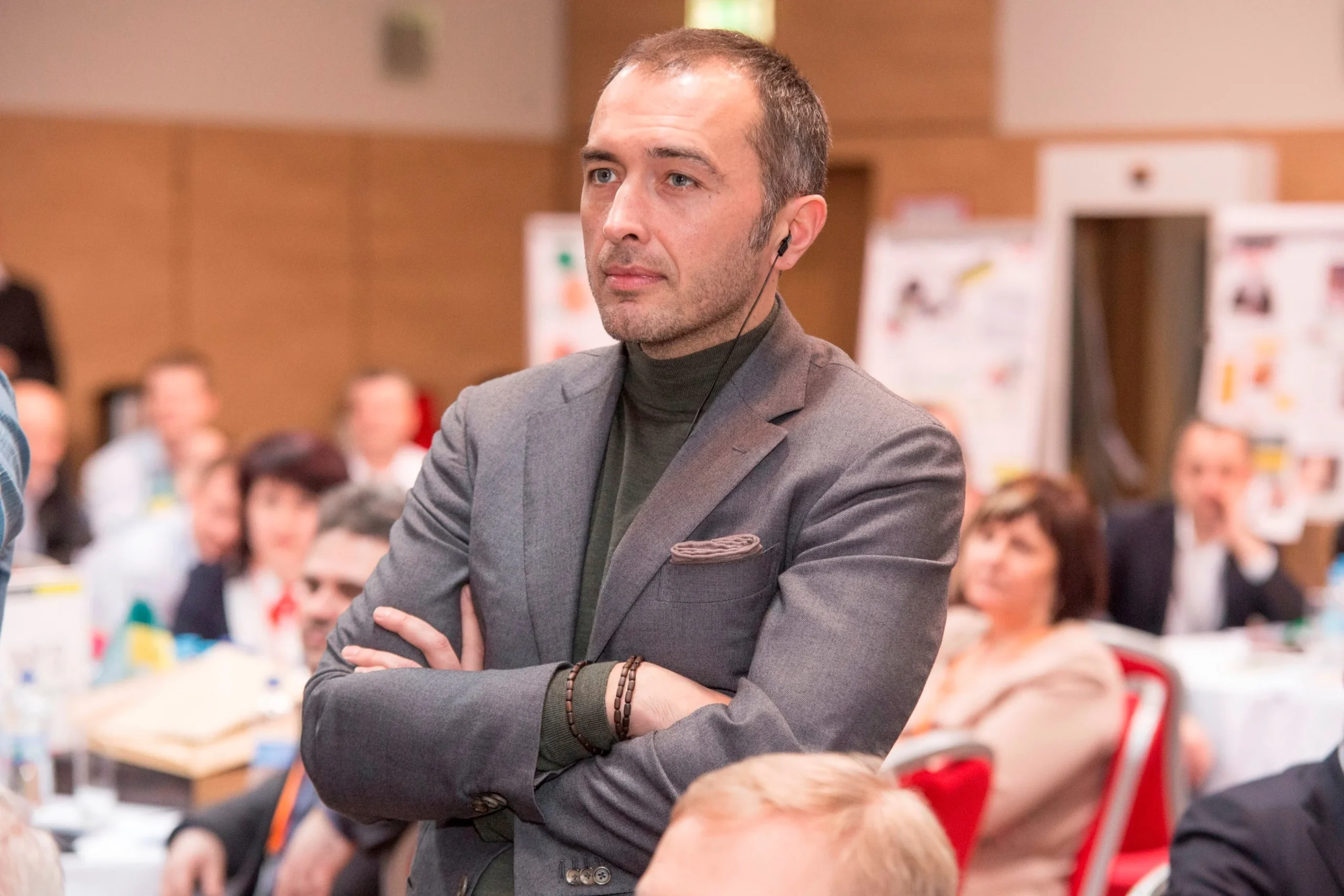 Чоловік у сірому піджаку зі схрещеними руками на конференції